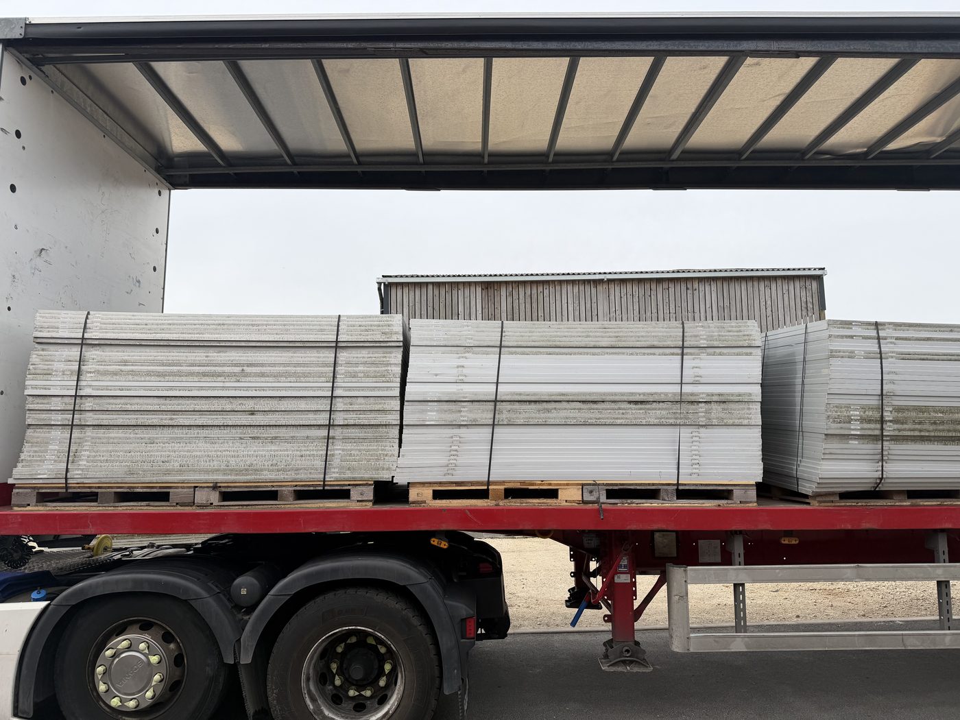 Pallets of decommissioned solar panels loaded onto a flatbed trailer at a farm site for recycling collection